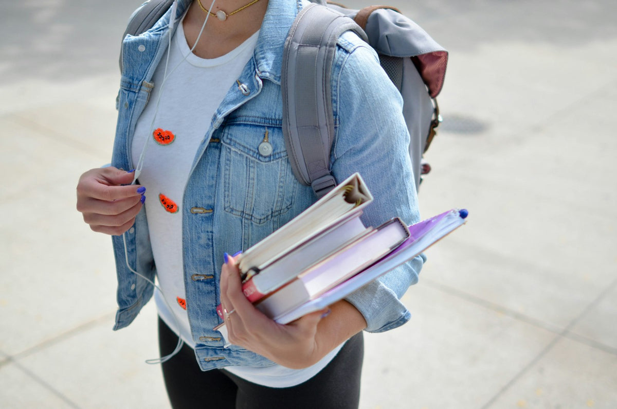 Student holding a book with a pack on one shoulder
