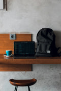 Backpack on a desk beside a laptop and a mug
