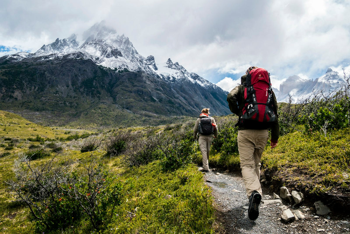 Two people walking towards a snow covered mountain