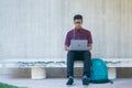 Person seated outdoors with a bag and a laptop