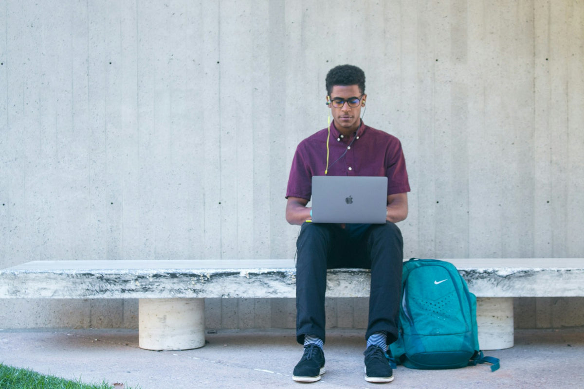 Person seated outdoors with a bag and a laptop